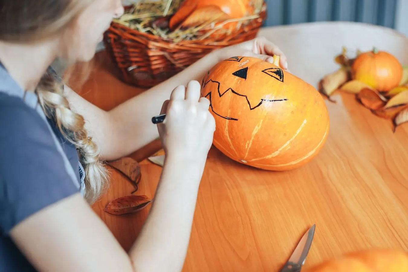 a girl drawing on a pumpkin with sharpie trick or treating murder mystery holiday parties halloween activities decorating party candy halloween party ideas