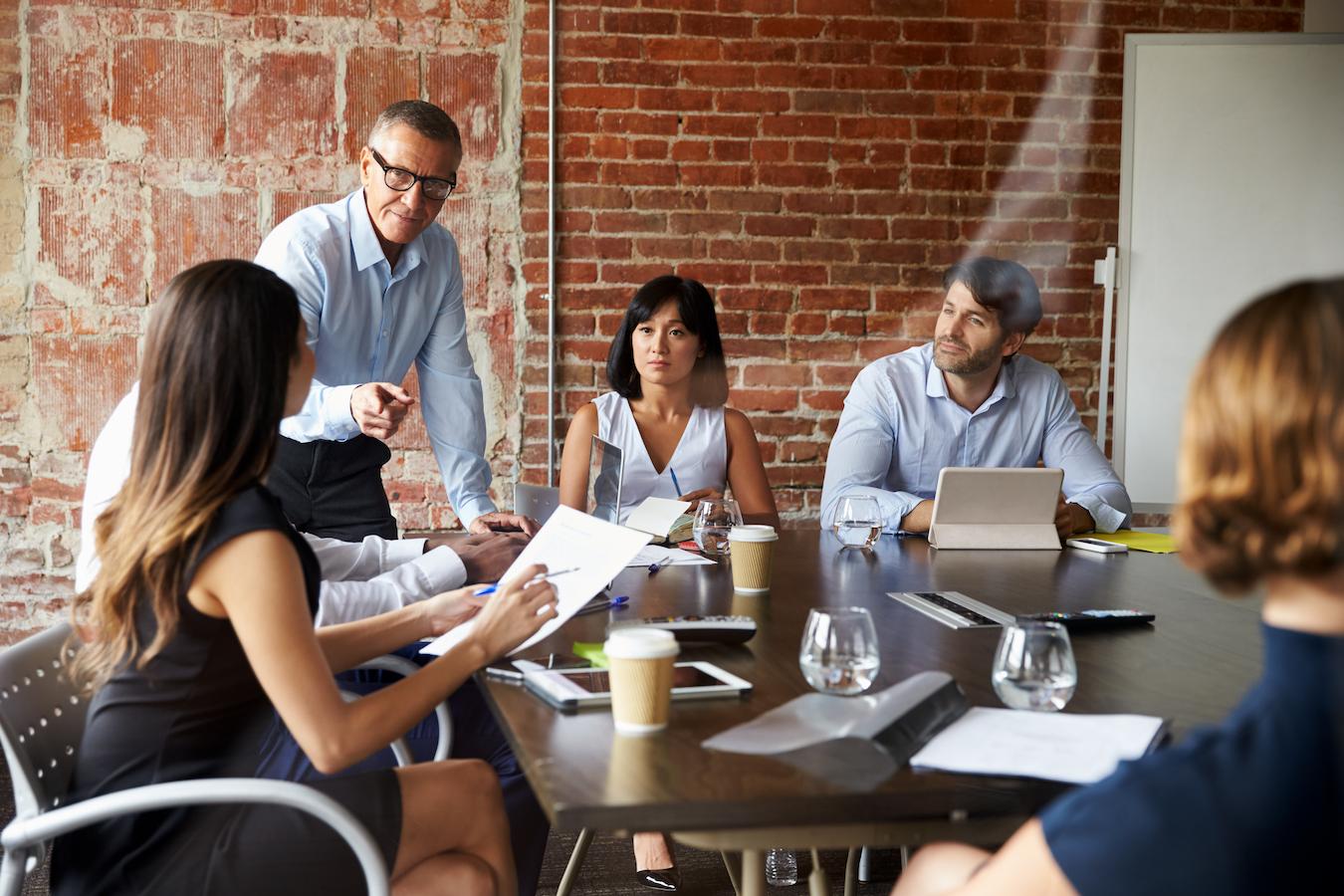 Business meeting at table in brick room where colleagues attend to schedule and address responsible leadership