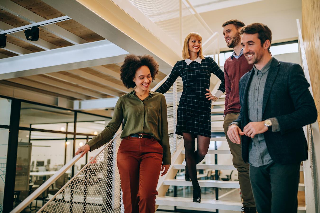 Four colleagues are building rapport as they walk down the stairs in an office and create a connection as they discuss shared business ideas
