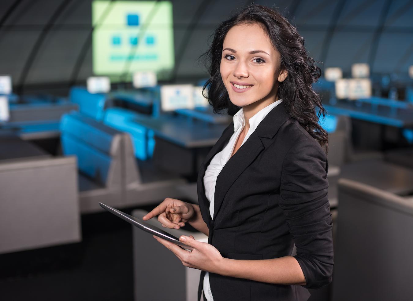 Hospitality management professional in white and black suit holds tablet and stands in a conference room for business meetings and other events