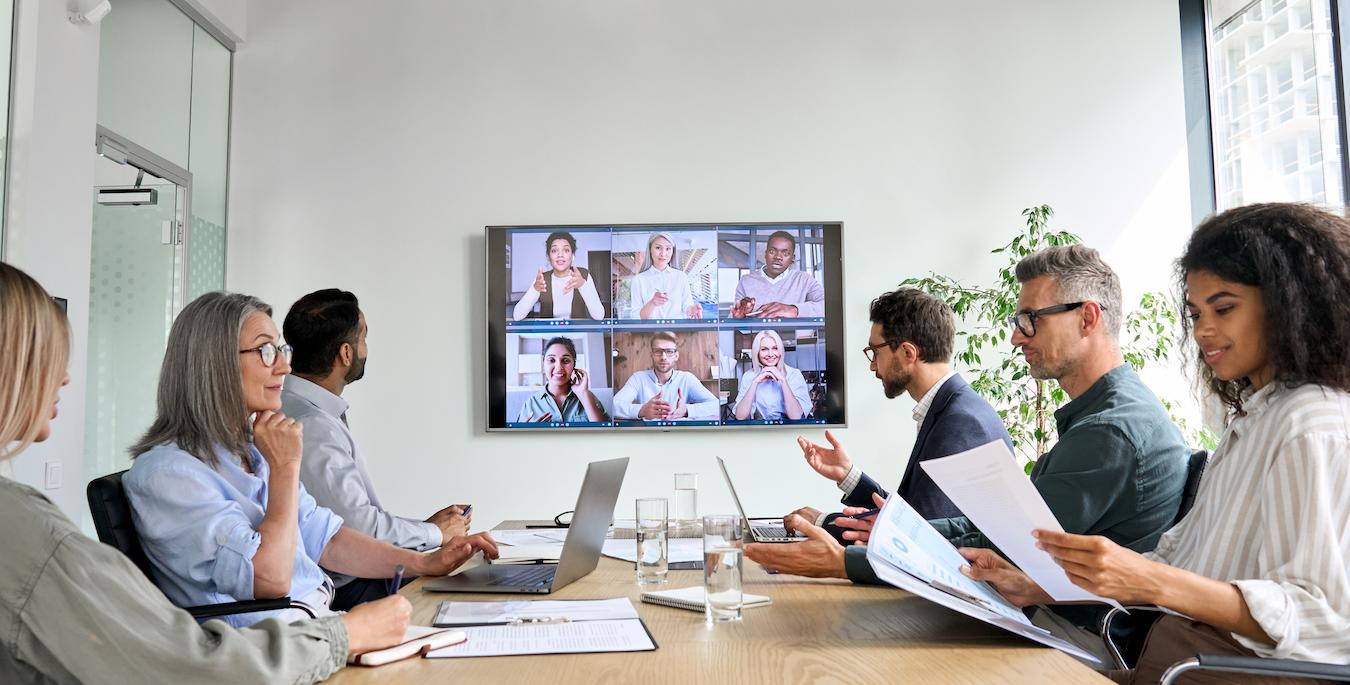 Meeting at productive business includes five colleagues in person and six on screen talking and taking notes on successful organizations