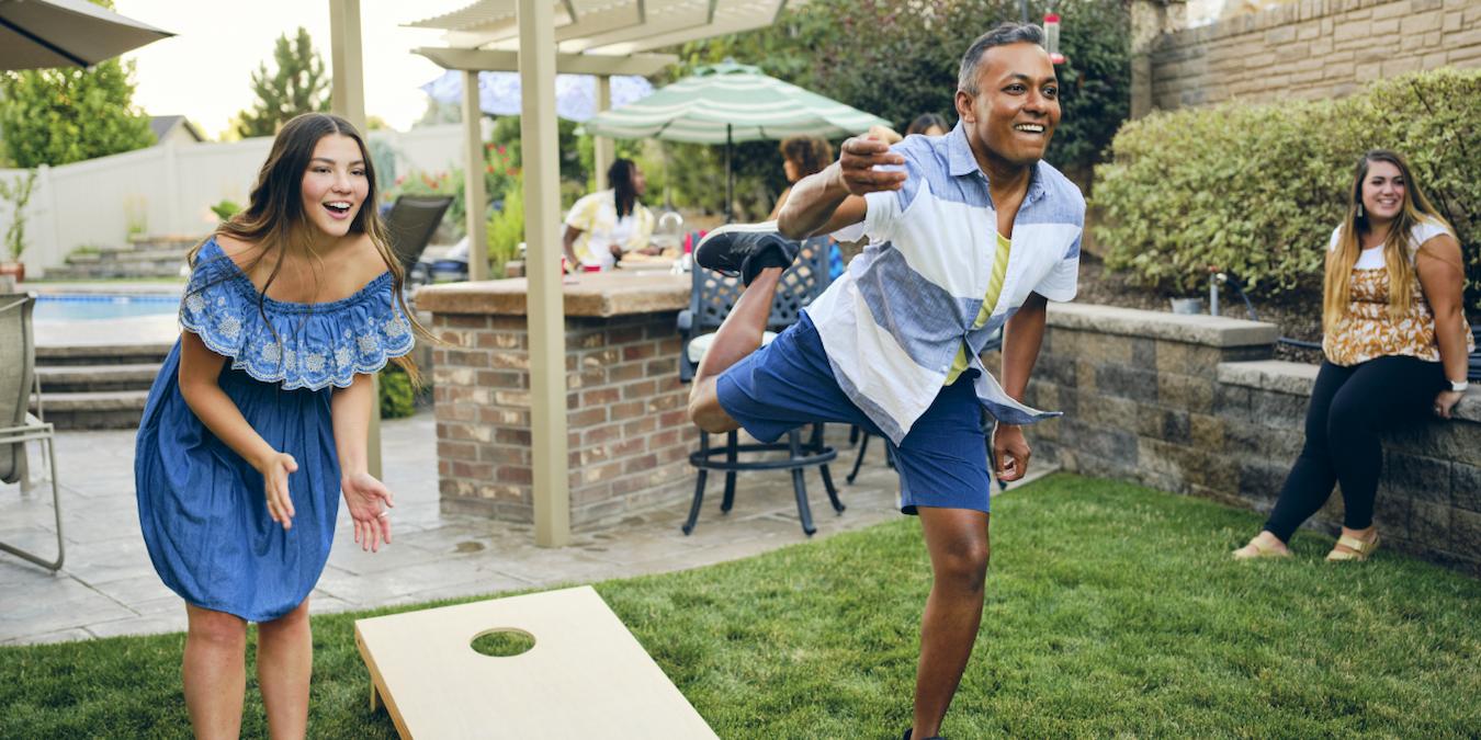 people playing a yard game outside at a gathering entire staff family members company picnic table federal holiday invite friends job satisfaction employees feel appreciated all the food hot dogs long weekend fair labor practices labor day weekend hard work ideas employees