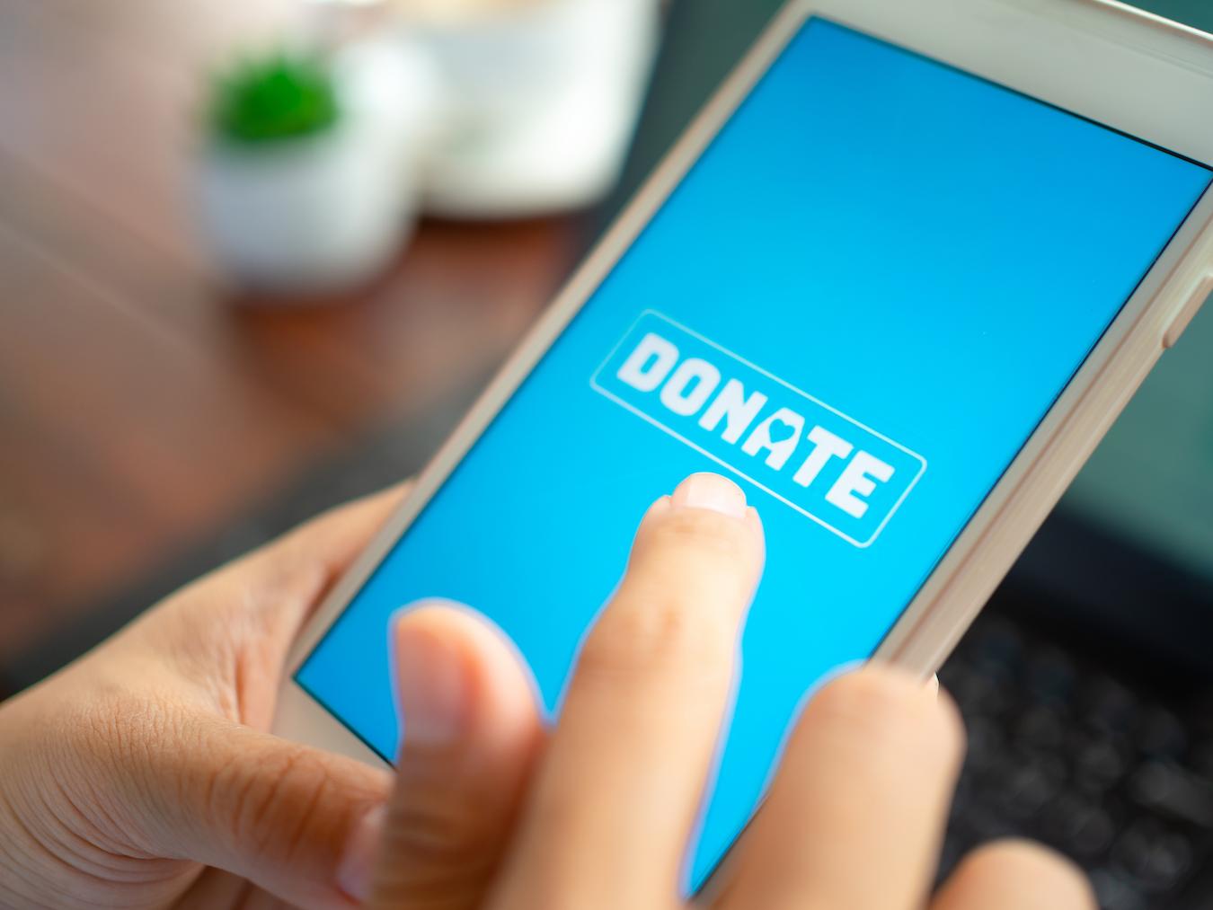 Person holds a smart phone and hovers their finger over the screen before making a donation