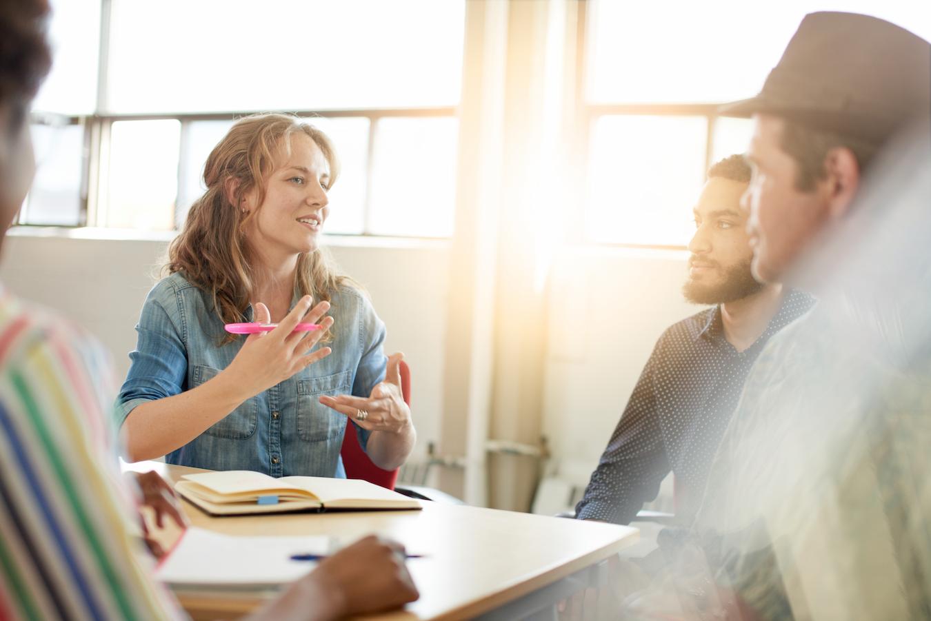 Person in denim button down uses a team meeting agenda template to lead three colleagues in current meeting