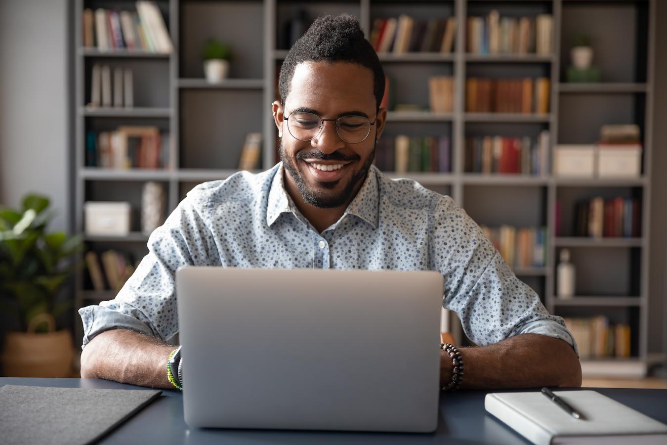 Person in dotted button down and glasses smiles as they type on their laptop