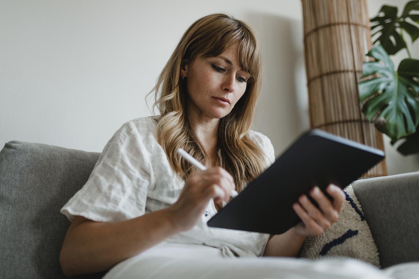 Person in white blouse sits down and uses tablet with stylus