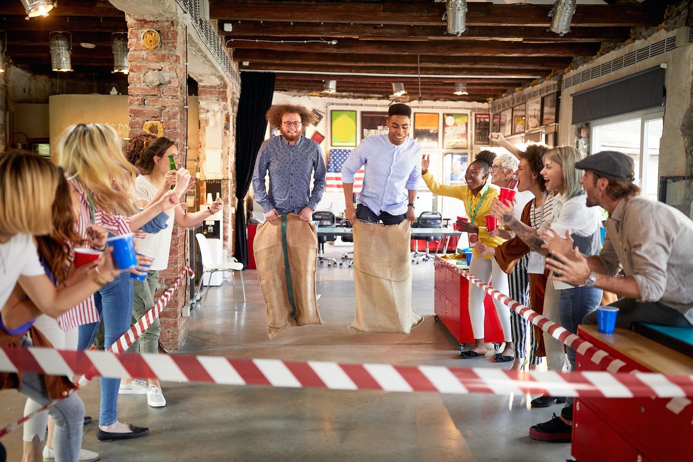 Potato sack race indoor employee engagement activity with two people competing and colleagues cheering from sidelines