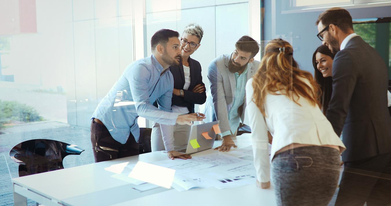 Six colleagues around table demonstrate the importance of team building as they get on the same page about their common goal